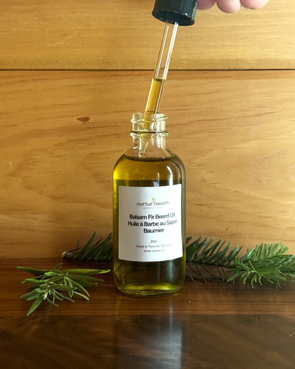 Glass dropper lifted from the bottle, holding the golden beard oil
