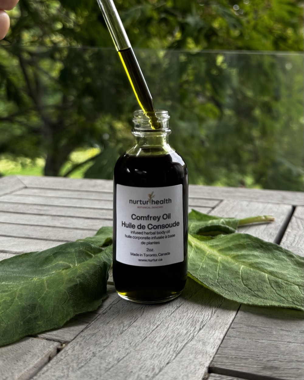 Glass dropper lifted from the bottle, holding the deep green infused oil