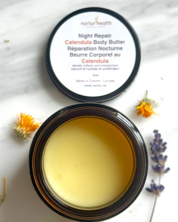 Open jar of night repair calendula body butter surrounded by dried calendula and lavender