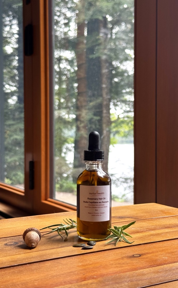 Rosemary Hair Oil on a table by a window overlooking the woods