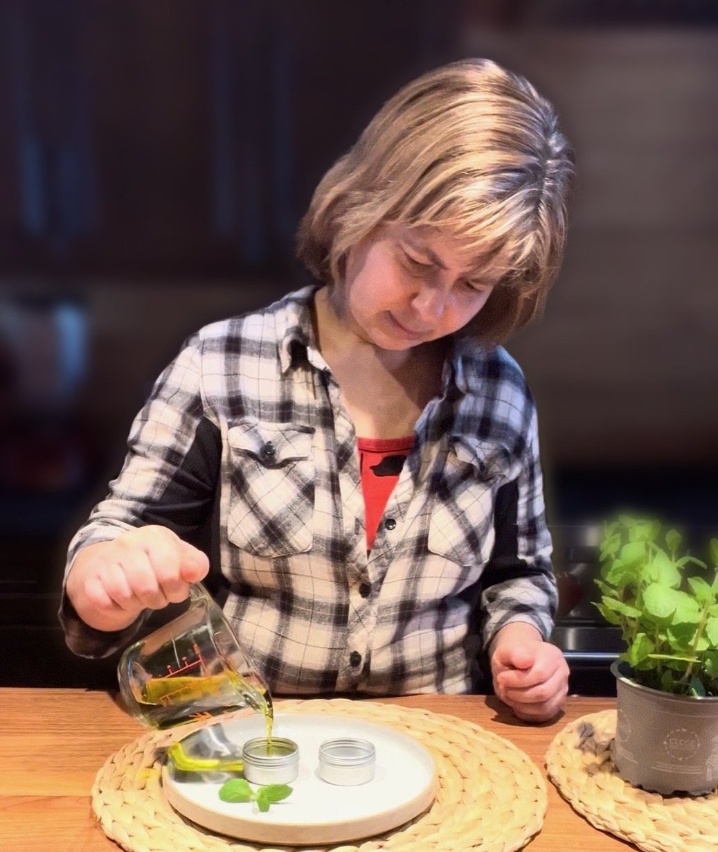 Olga at her workbench, pouring herbal oil into a salve tin
